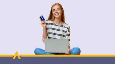 Uśmiechnięta młoda kobieta siedząca z laptopem i kartą płatniczą w ręce