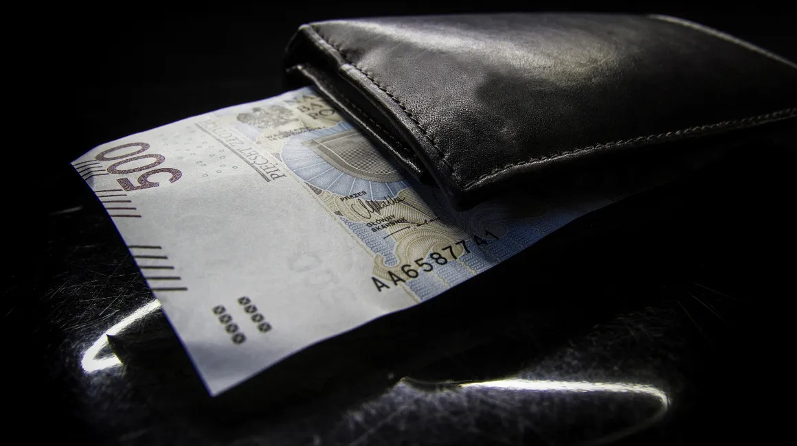 Banknot 500 złotych częściowo wysunięty z czarnego skórzanego portfela na ciemnym tle