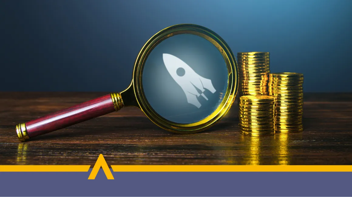 Lupa skierowana na ikonę rakiety obok stosów złotych monet