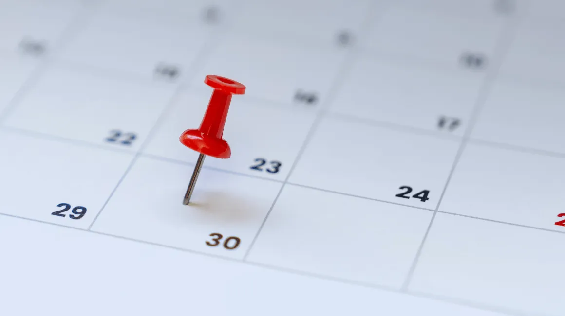 Czerwony pinezek wbity w kartkę kalendarza, zaznaczający trzydziesty dzień miesiąca